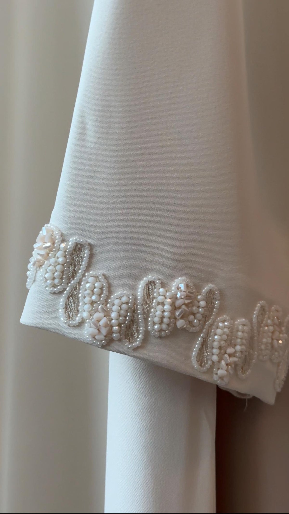 Close-up of a white or ivory fabric garment sleeve with ornate beaded and embroidered cuff detailing in white and pale pink tones.