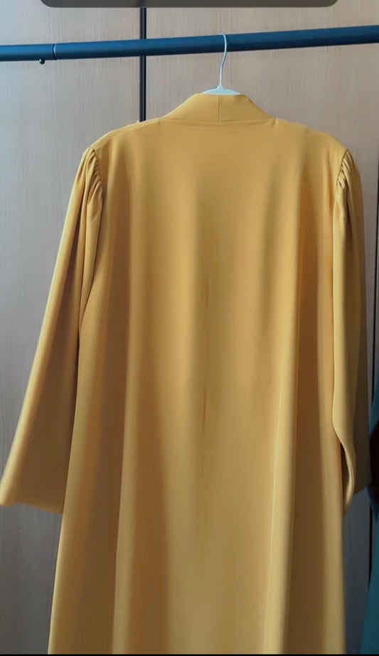 A mustard yellow long-sleeve dress or tunic hanging on a white hanger against a light gray wall with a blue clothing rack bar visible at the top.