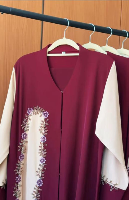 Burgundy Blossom Abaya featuring a rich burgundy body, contrasting ivory panels and sleeves, with hand-beaded floral embroidery in lavender, silver, and crystal accents.
