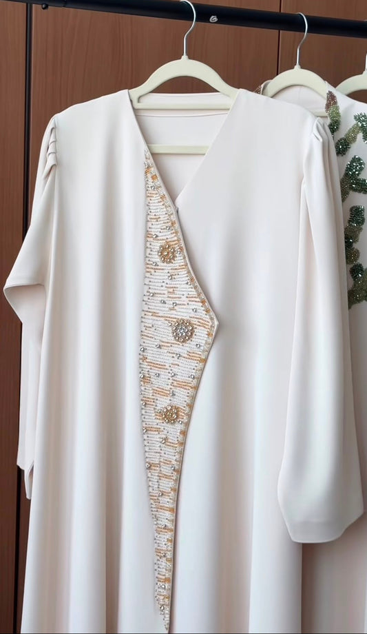 Champagne Royale Abaya in ivory white featuring a handcrafted champagne gold crystal embellished front panel with a graceful flowing silhouette.