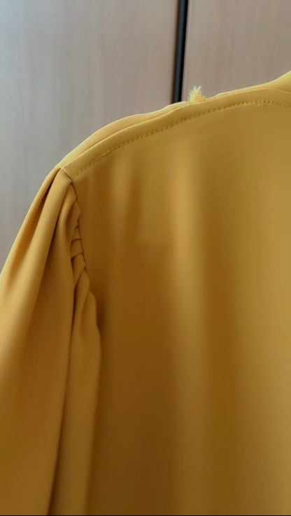 Close-up of a mustard yellow garment, showing the shoulder seam, sleeve attachment, and fabric texture.