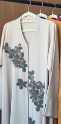Elegant Sage Blossom Abaya in ivory beige with hand-beaded sage green floral appliqués and front zip closure.