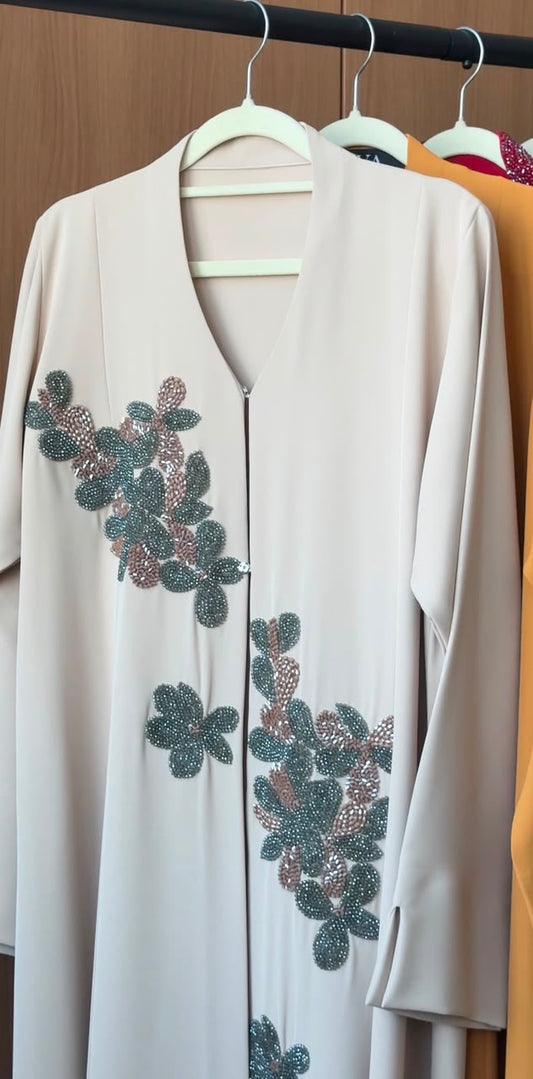 Elegant Sage Blossom Abaya in ivory beige with hand-beaded sage green floral appliqués and front zip closure.
