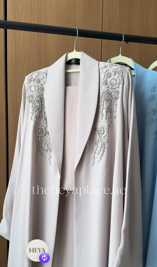 Silver Blossom Abaya in pearl beige featuring intricate silver floral embroidery on the shoulders, an elegant shawl collar, and a flowing luxury silhouette.